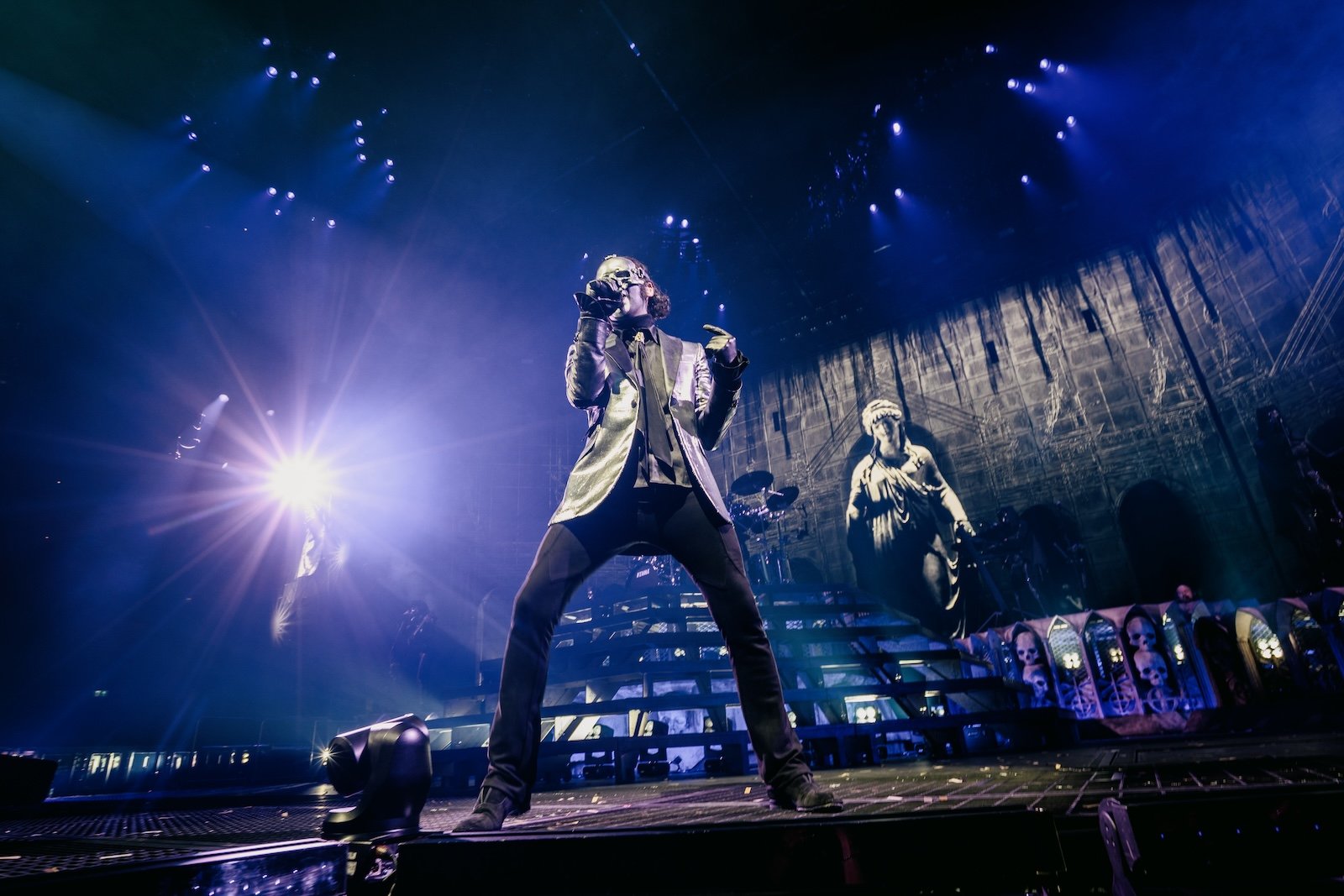 Members of Ghost performing live on stage, wearing their signature costumes and masks, with dramatic lighting and stage effects.