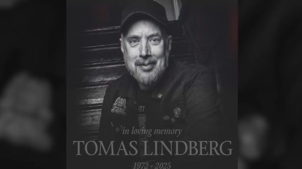 Black-and-white memorial portrait of Tomas Lindberg wearing a cap and jacket, seated on a staircase, with the text “In loving memory Tomas Lindberg 1972–2025.”
