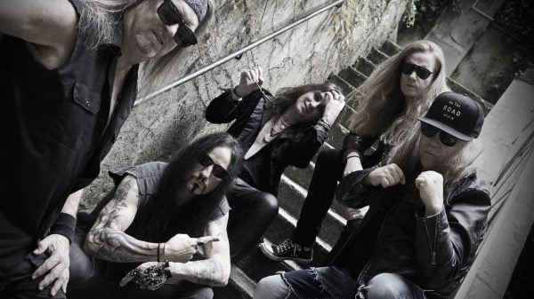 Five members of the heavy metal band Vicious Rumors posing on a staircase in a 2025 professional band photo, all holding serious expressions and wearing rock‑style attire.