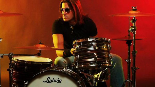 Joey Cassata sitting behind his drum kit in a promotional photo.
