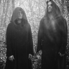The two members of Sunn O))) standing side by side in black-and-white, wearing long robes, in a minimalist, dramatic composition.