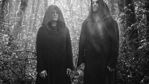 The two members of Sunn O))) standing side by side in black-and-white, wearing long robes, in a minimalist, dramatic composition.